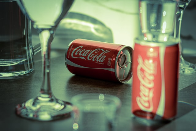  En närbild på ett bord som är dukat med glas och två Coca-Cola burkar varav en är liggande och en är stående 