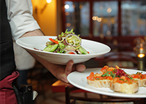 Mysig Restaurangmiljö med en servitör som bär in två vita tallrikar en med sallad och en med bruschetta 