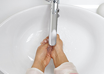 En person som tvättar händerna med Tvål under rinnande vatten från en modern silverkran i ett vitt handfat.