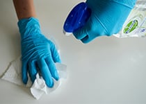 Två händer rengör en golvyta med rengöringsmedel och torkpapper