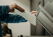 En person i en jeansskjorta som använder konstorsmaterial för att skanna eller kopiera dokument i en kontorsmiljö.