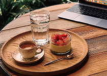 Träbord med en rund bricka, på brickan är det en kopp med fat, en glasbägare med ljus fyllning och jordgubbar samt ett  glas vatten