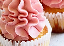 Muffins förpackad i en vit muffinsform. Muffinsen är ljus och har rosa frosting som går i ett vågigt mönster rakt uppåt.