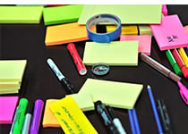 Färgglada post-it-lappar, pennor, markörer och en tejprulle utspridda över en svart yta i en reception. 