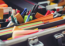 Ett färgstarkt sortiment av kontorsmaterial inklusive pennor, markörer, gem och klisterlappar  organiserade i en öppen portfölj.