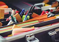 Färgglada post-it-lappar, pennor, markörer och en tejprulle utspridda över en svart yta på ett skrivbord.