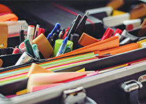 Färgglada post-it-lappar, pennor, markörer och en tejprulle utspridda över en svart yta på ett skrivbord.