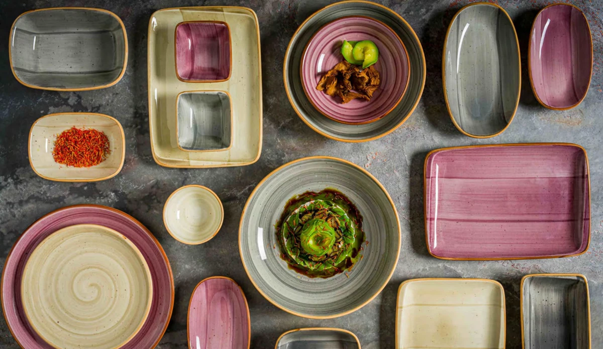 Tallrikar och skålar i grått, beige och rosa keramik placerade på ett mörkt bord.