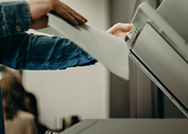 En person i en jeansskjorta som använder konstorsmaterial för att skanna eller kopiera dokument i en kopieringsmaskin. 